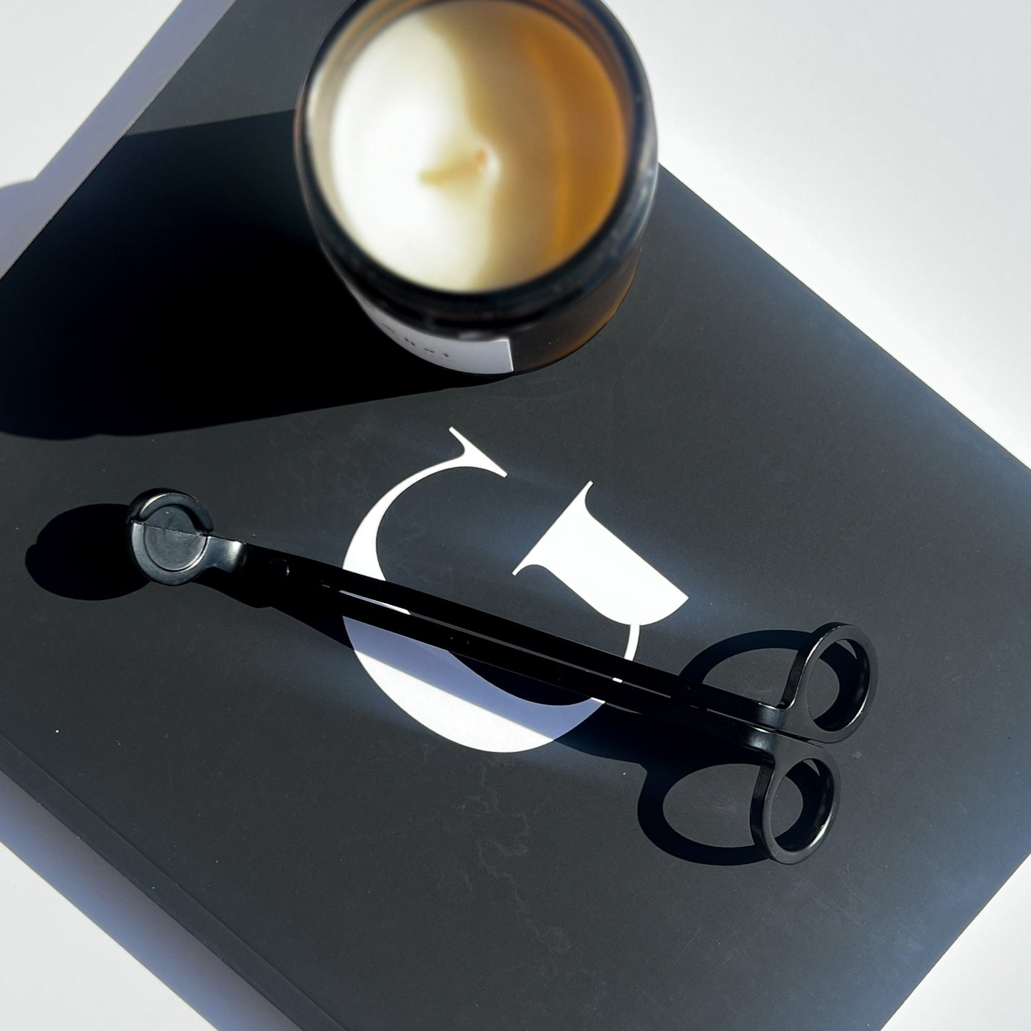 matte black wick trimmer with candle sitting on notebook