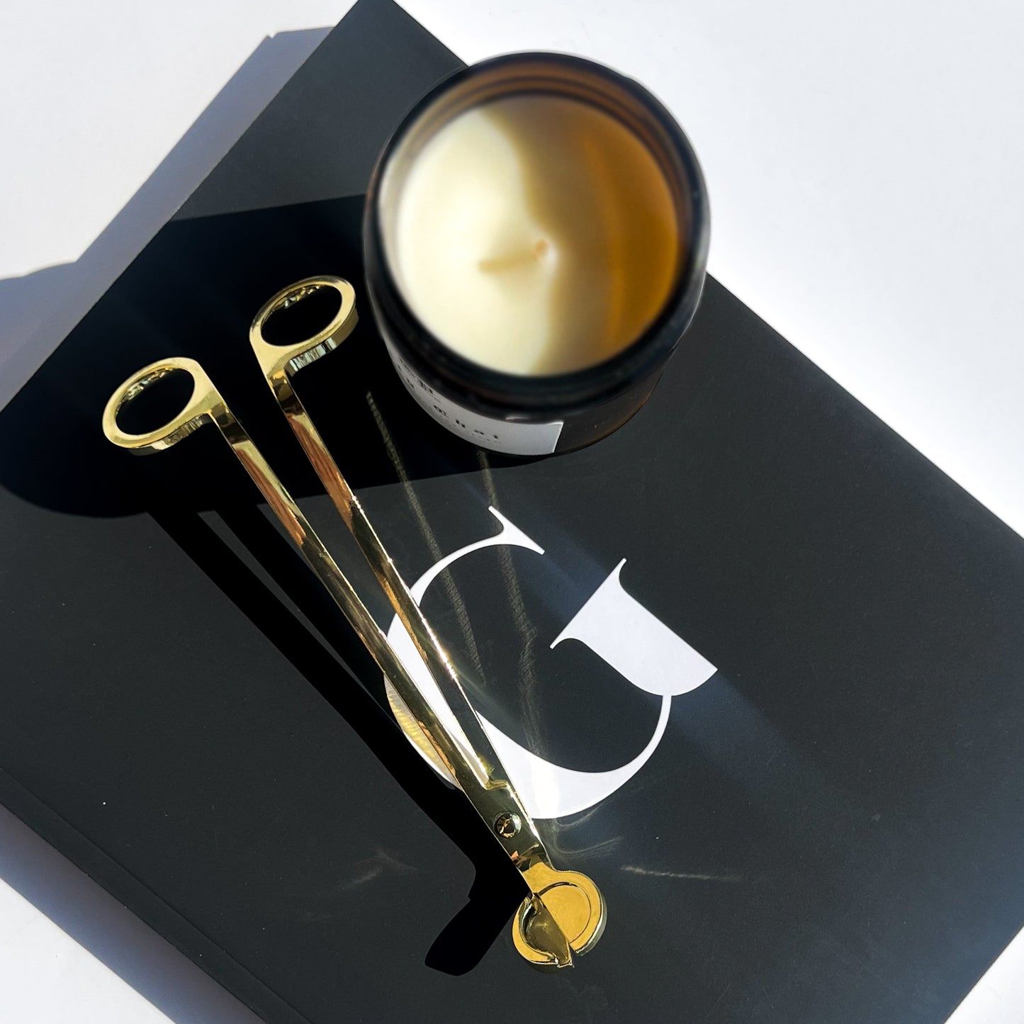 gold wick trimmer next to candle on notebook