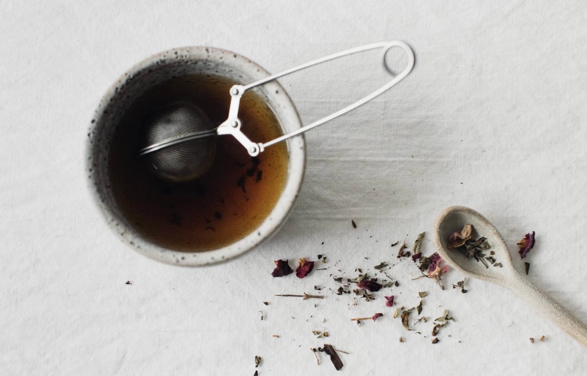 Cup of aesthete tea with diffuser in white teacup on white background