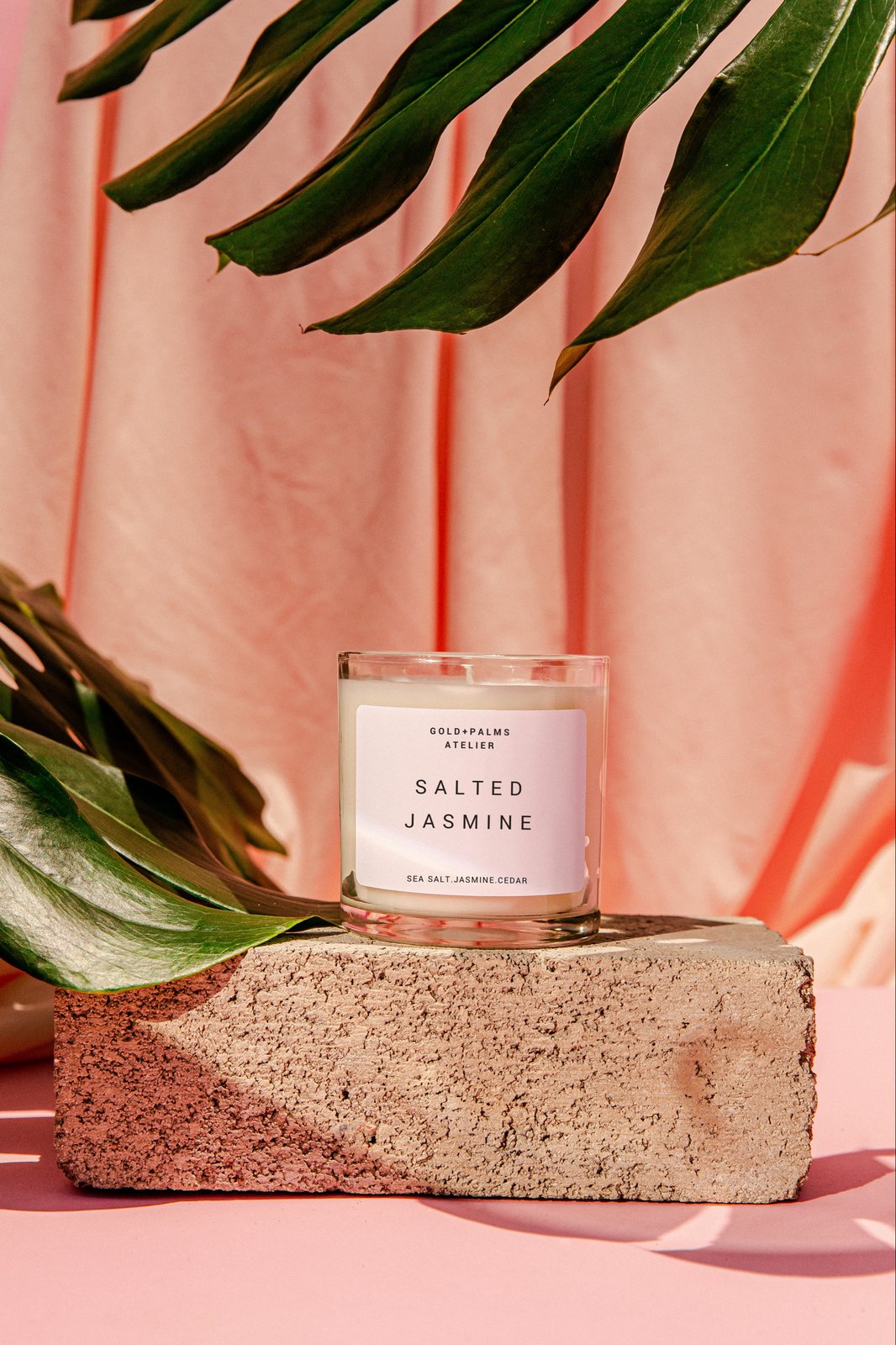 Salted air and Jasmine scented soy candle in clear vessel with pink tropical background