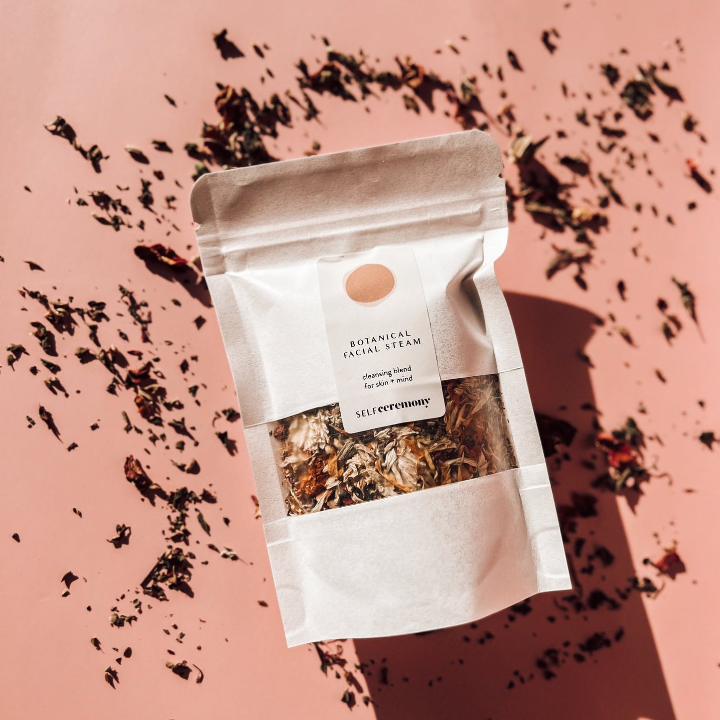 facial steam in white package with crushed petals and a pink bakckground