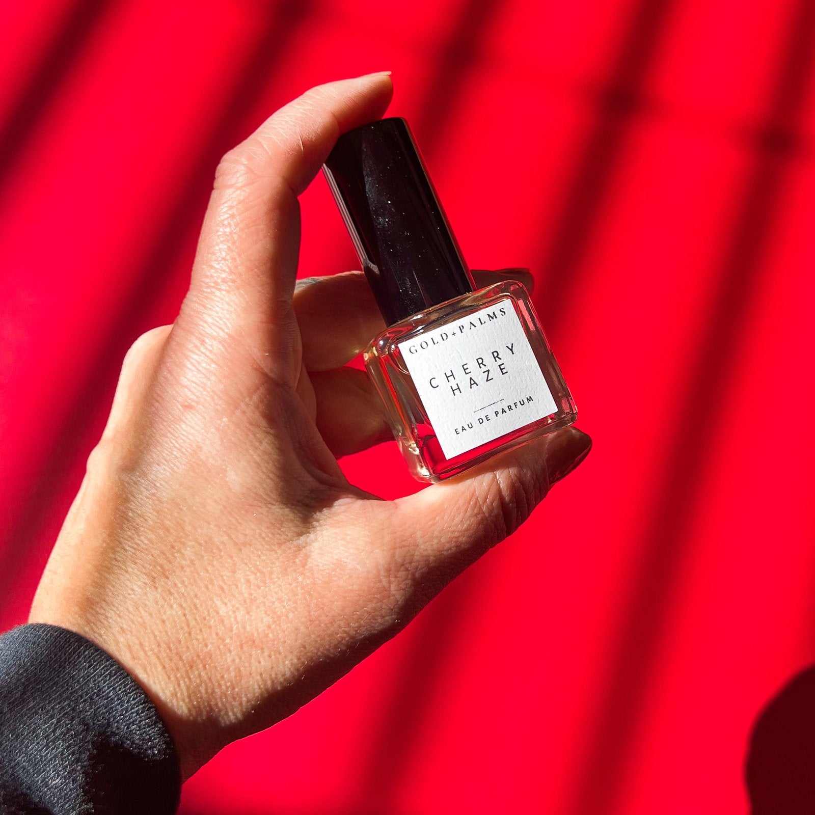 hand holding smokey cherry vanilla eau de parfum 15 ml with red background
