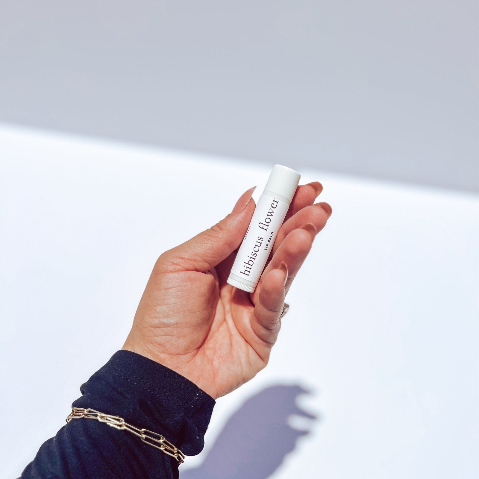 luxe lip balm hibiscus flower held against white background