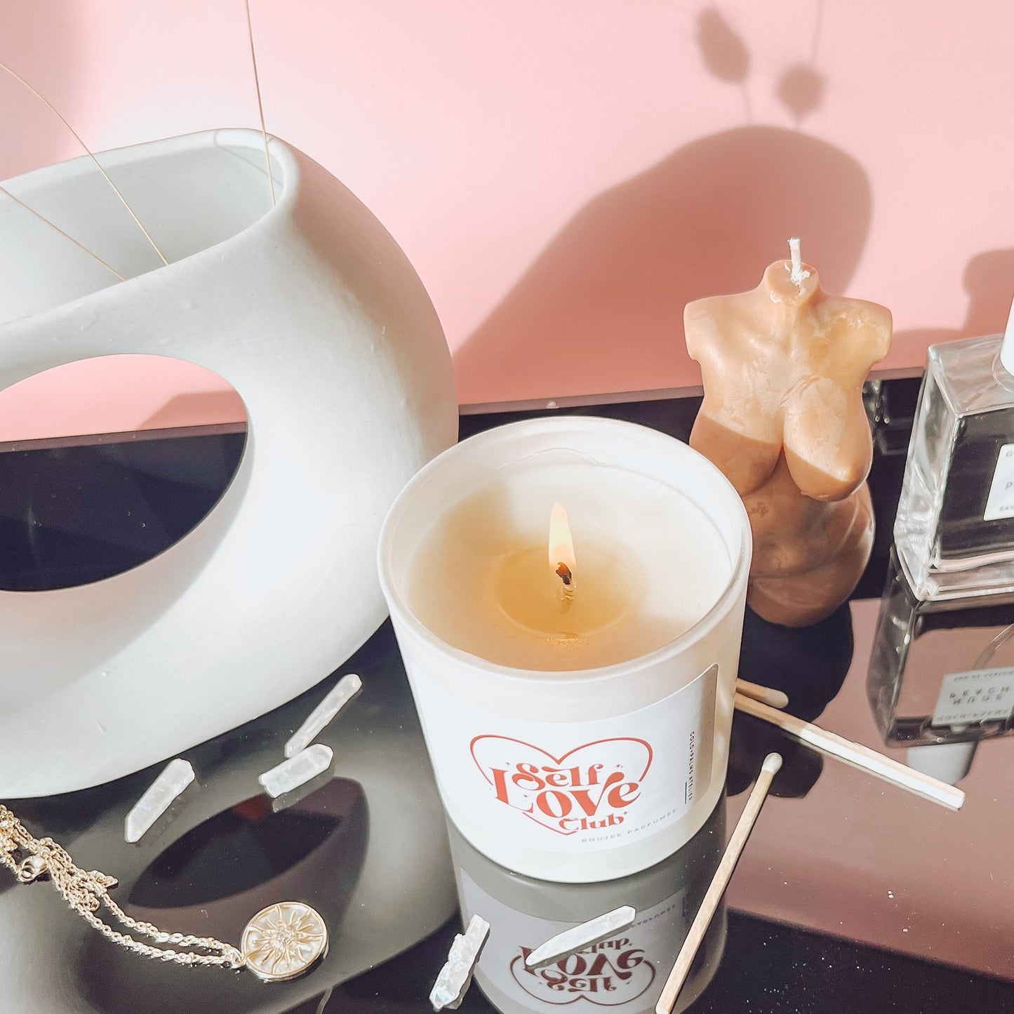 self love candle lit with pink background and crystal on a counter